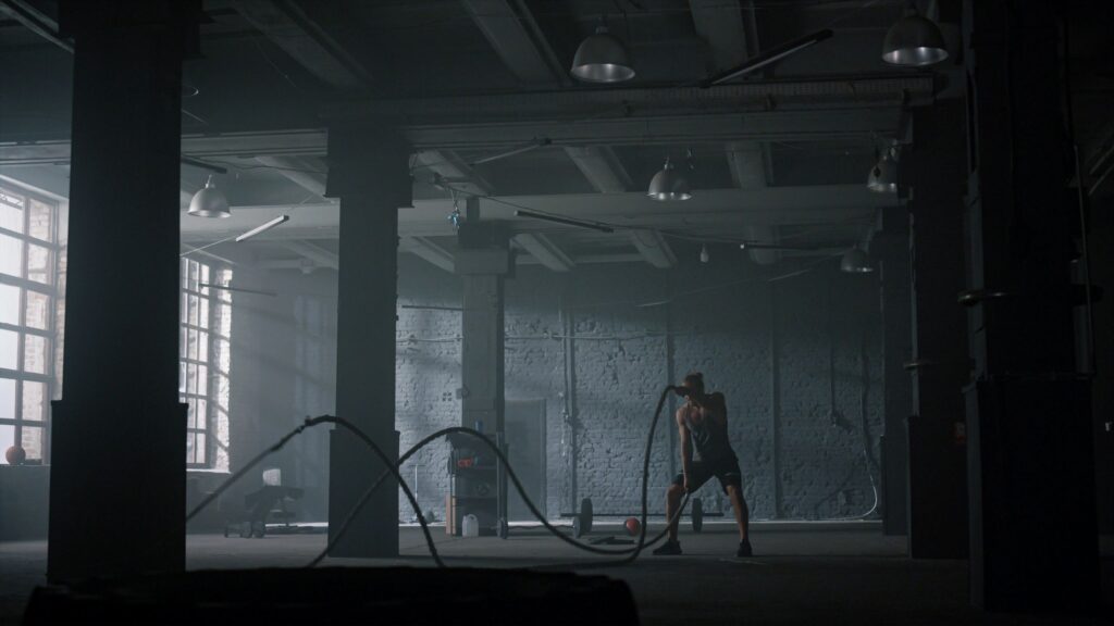 Guy battling ropes in gym. Athletic man doing gym workout in loft building